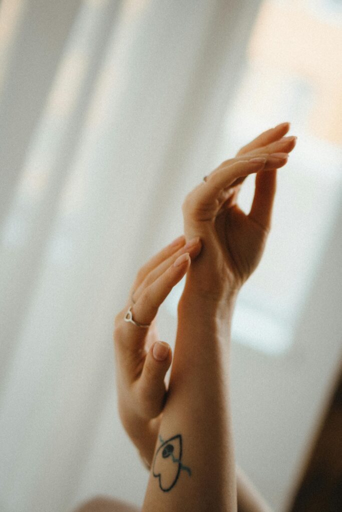 Close-up of elegant hands with a tattoo, delicately touching in soft light.